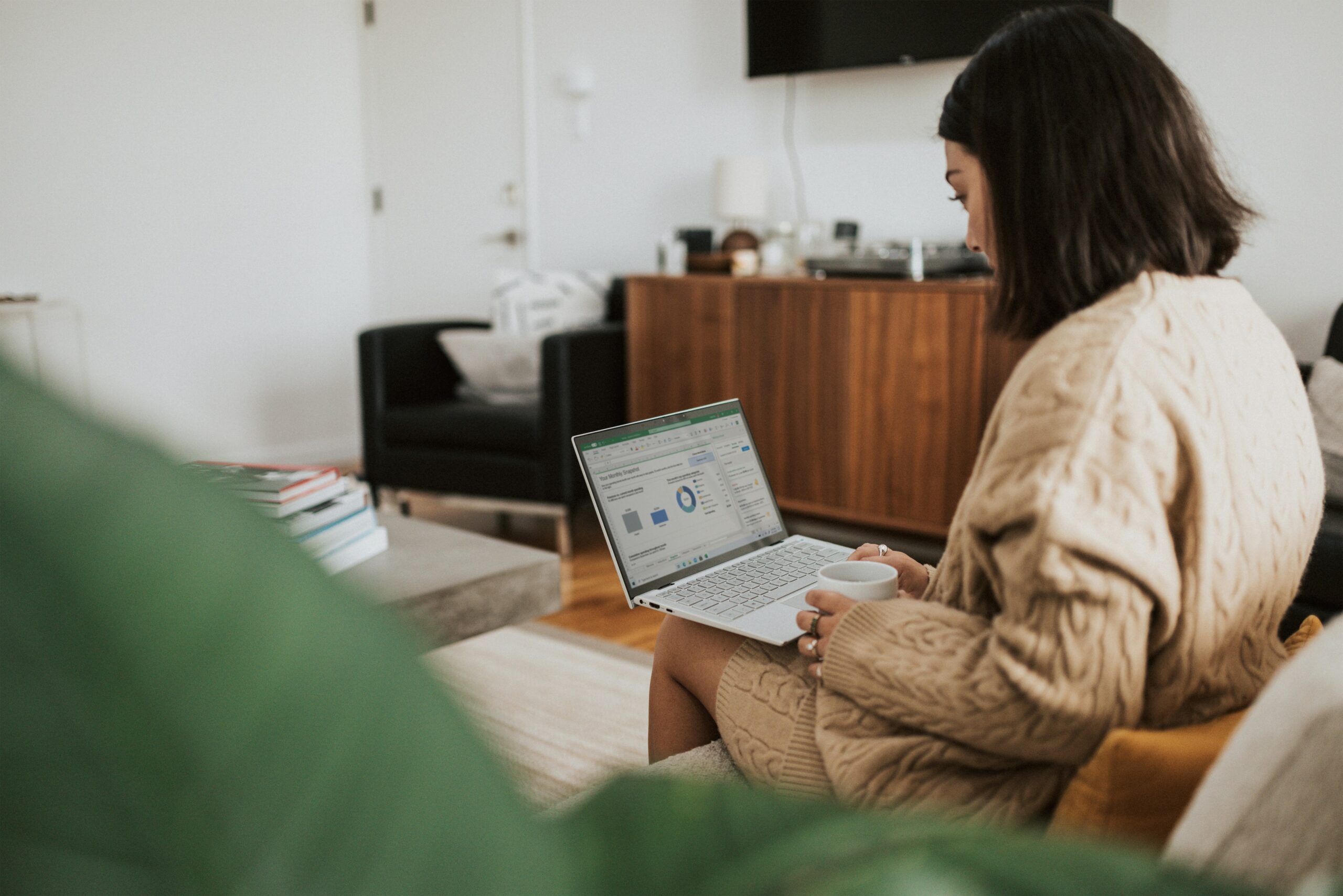 Woman in brown jacket on laptop looking at a monthly chart on screen.